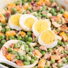 Close up with pea salad with eggs laying on top with a spoon about to scoop out a bunch.