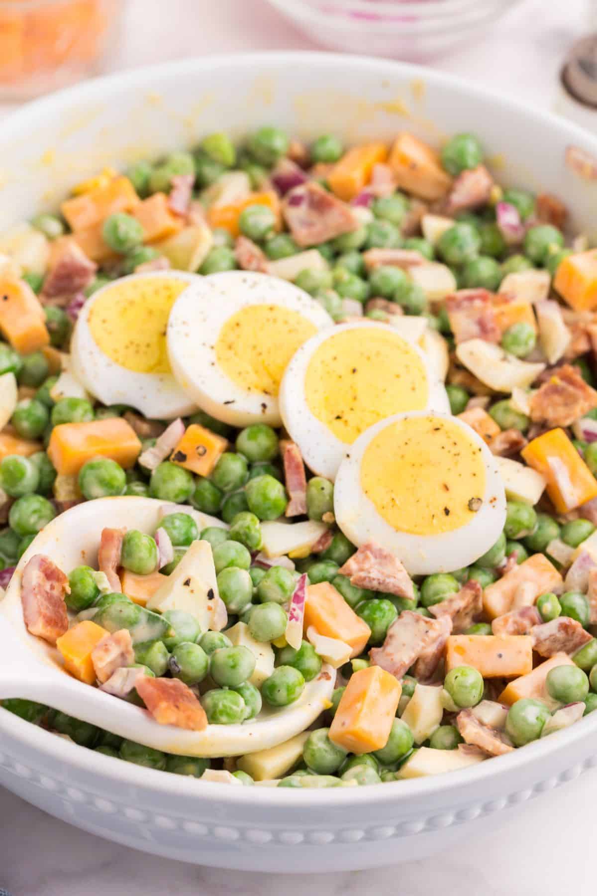 Close up with pea salad with eggs laying on top with a spoon about to scoop out a bunch.