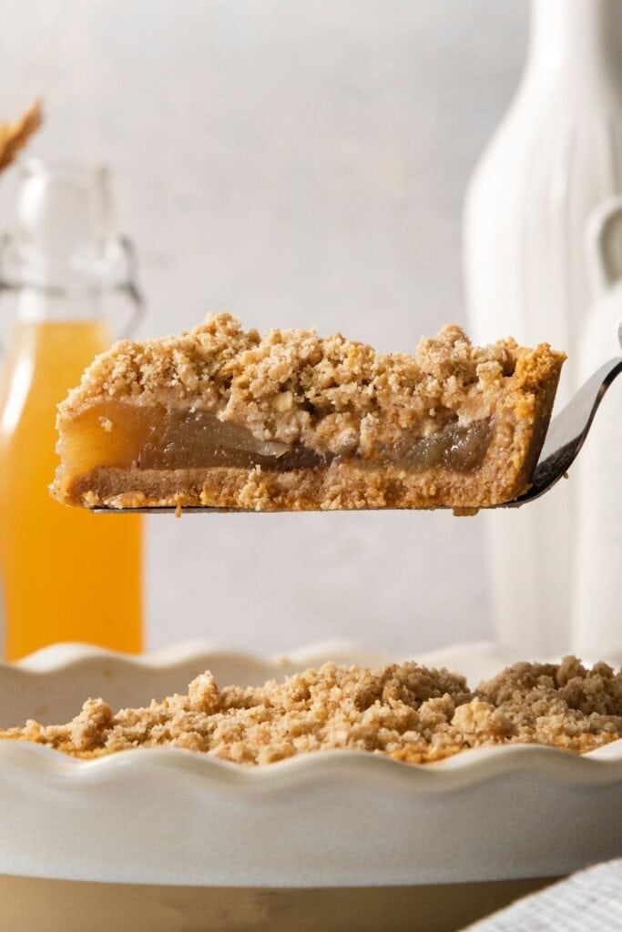 A slice of the no bake apple pie being held up over the pie crust at a side angle to see inside the pie.