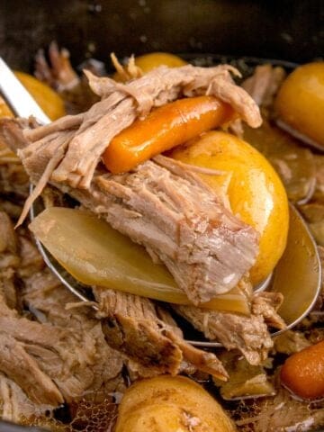 Close up of the sirloin tip roast in the crock pot being picked up with a spoon with carrots and baby potatoes.
