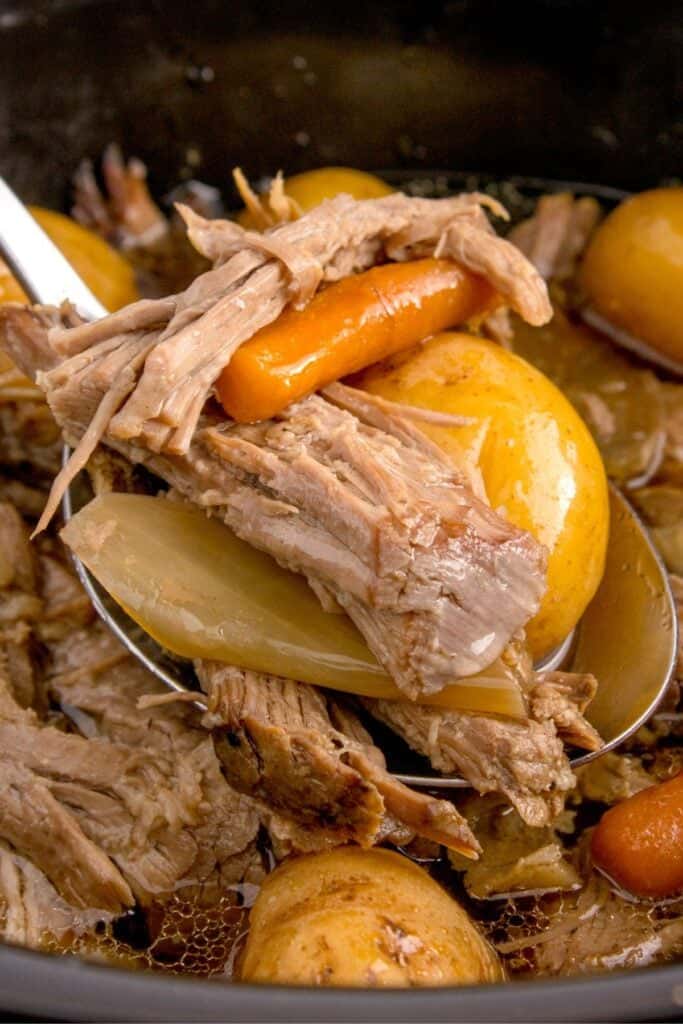 Close up of the sirloin tip roast in the crock pot being picked up with a spoon with carrots and baby potatoes.