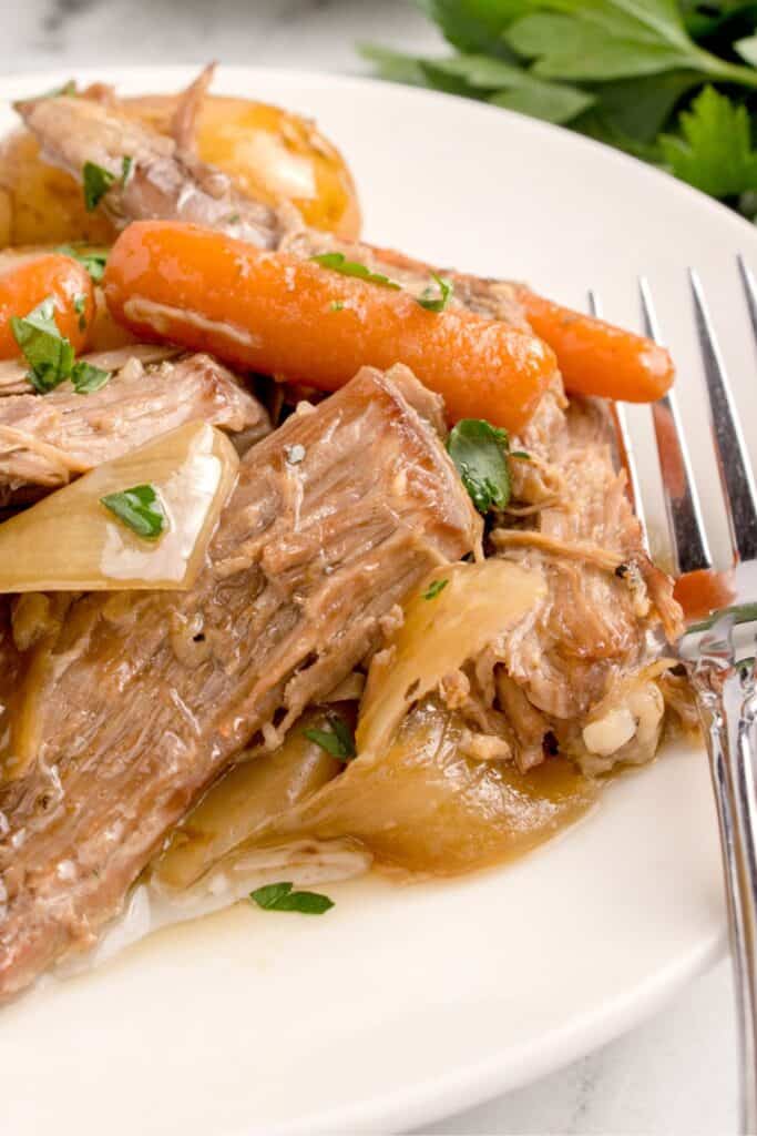 Close up of the slow cooker sirloin tip roast on a plate with a fork to the side.
