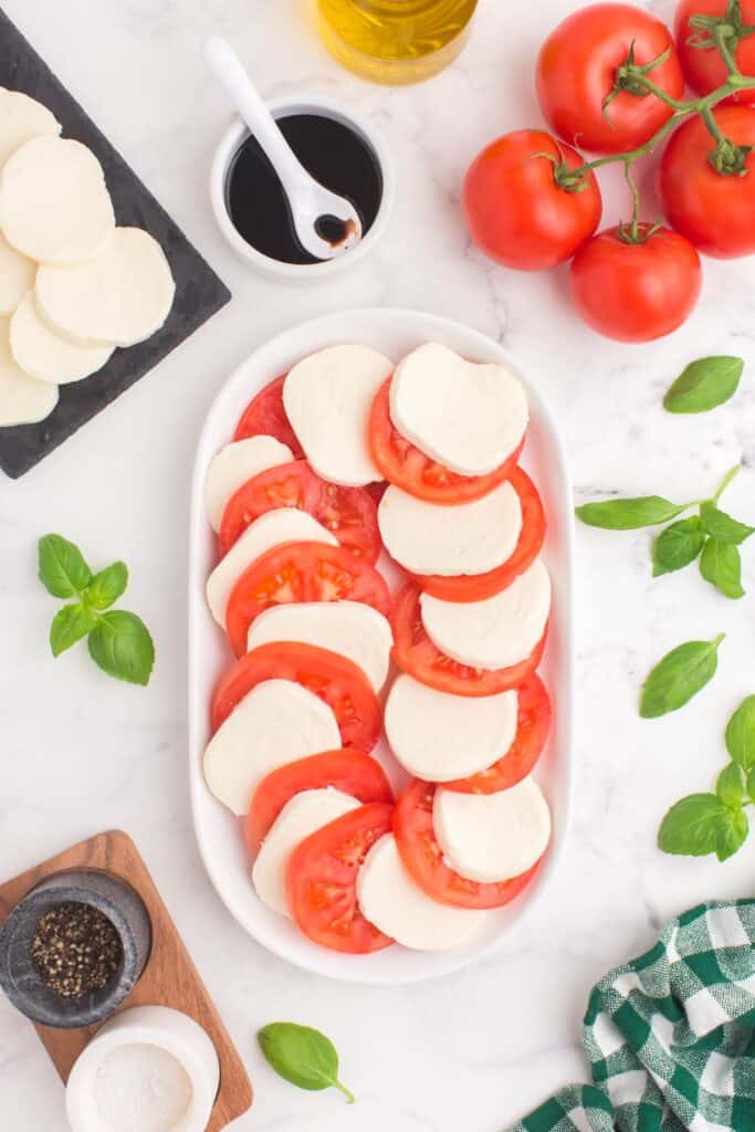 adding sliced mozzarella cheese and tomato slices on a white platter