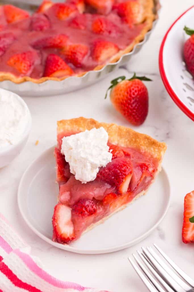 fresh strawberry pie slice on a white plate with whipped cream
