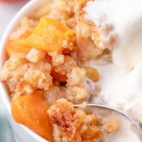 close up of peach cobbler cake with ice cream and peach chunks