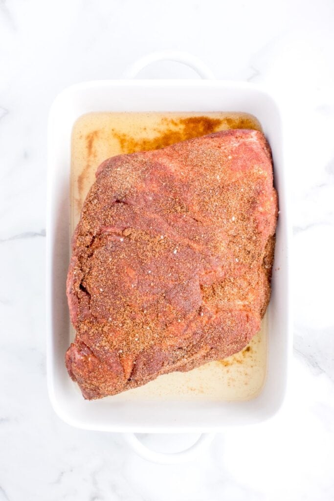 pouring in chicken broth over seasoned pork shoulder