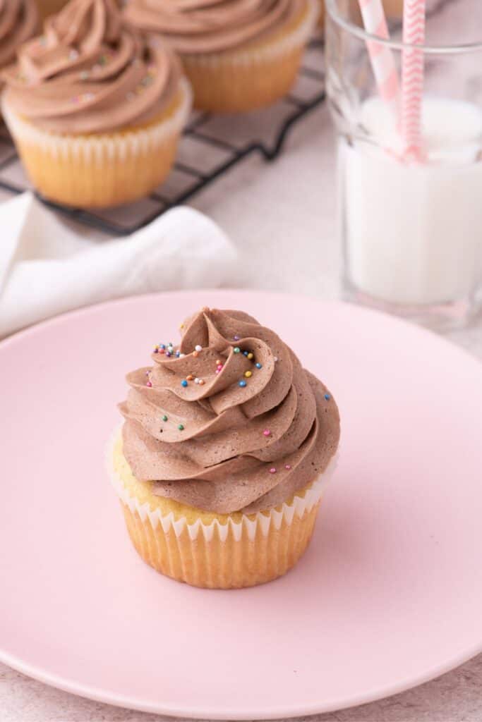 single homemade cupcake on a pink plate with a glass of milk