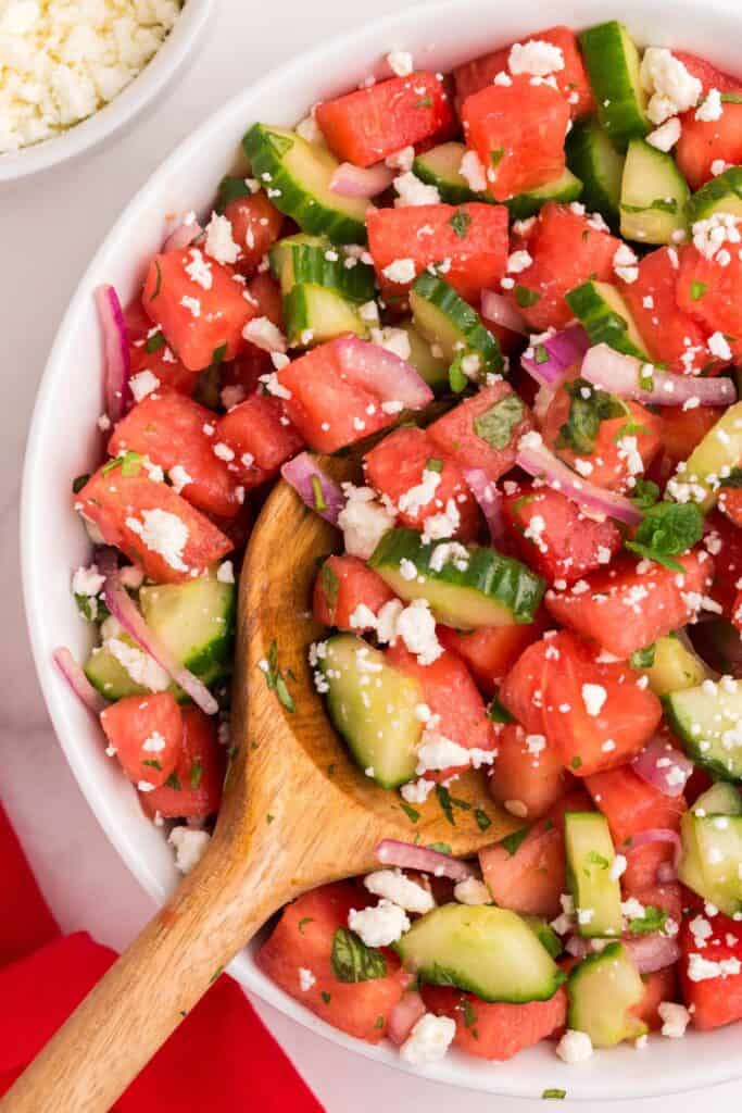 tossing watermelon salad with salad spoons and serving in bowls 