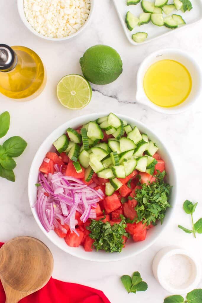combining watermelon, cucumber and red onion in a salad bowl 