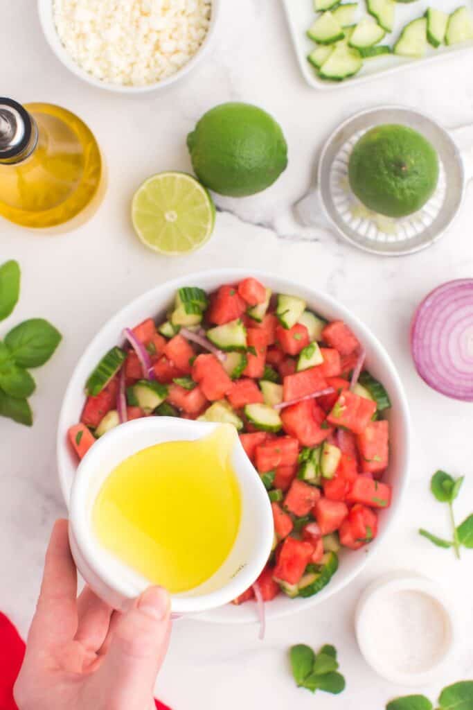 pouring lime and olive oil vinaigrette over watermelon salad 