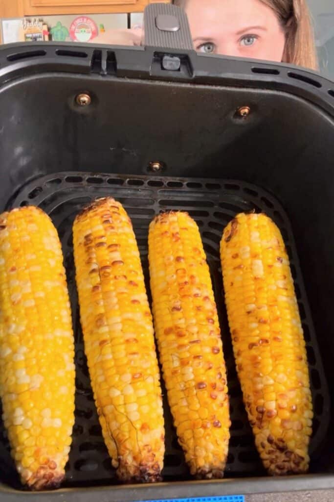 Woman holding up an air fryer basket full of air fryer corn on the cob.