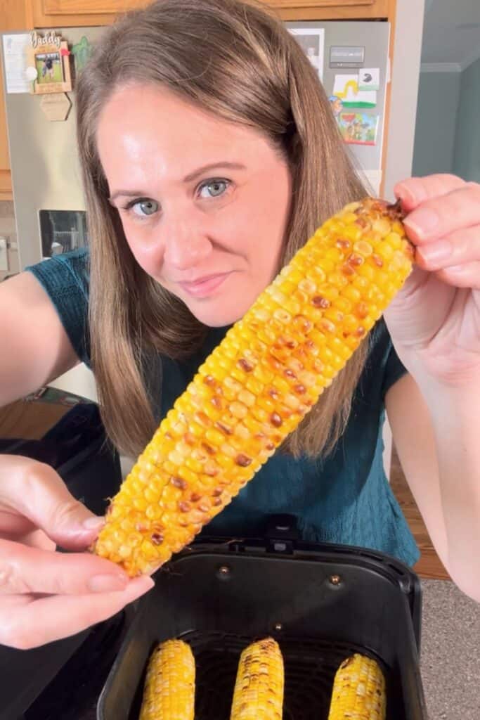 Woman (me) holding a piece of air fryer corn on the cob with hands toward the camera to see the roasted spots.