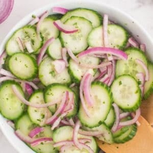 Closeup of the cucumber and onion salad in a serving bowl with wooden serving utensils.