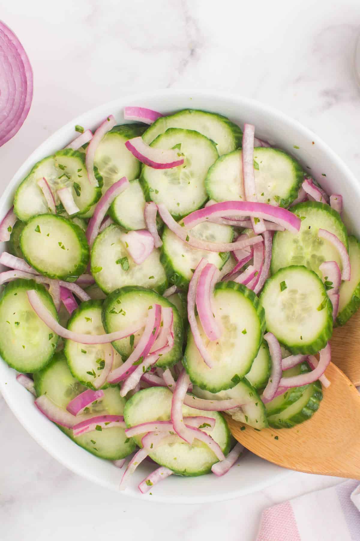 Closeup of the cucumber and onion salad in a serving bowl with wooden serving utensils.