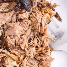Oven roasted pulled pork cooked and being shredded with a fork on a plate.