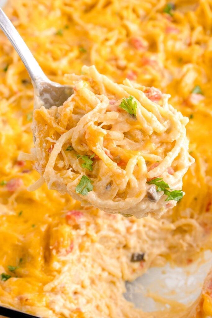 Using a slotted spoon to serve chicken spaghetti with rotel onto a plate.