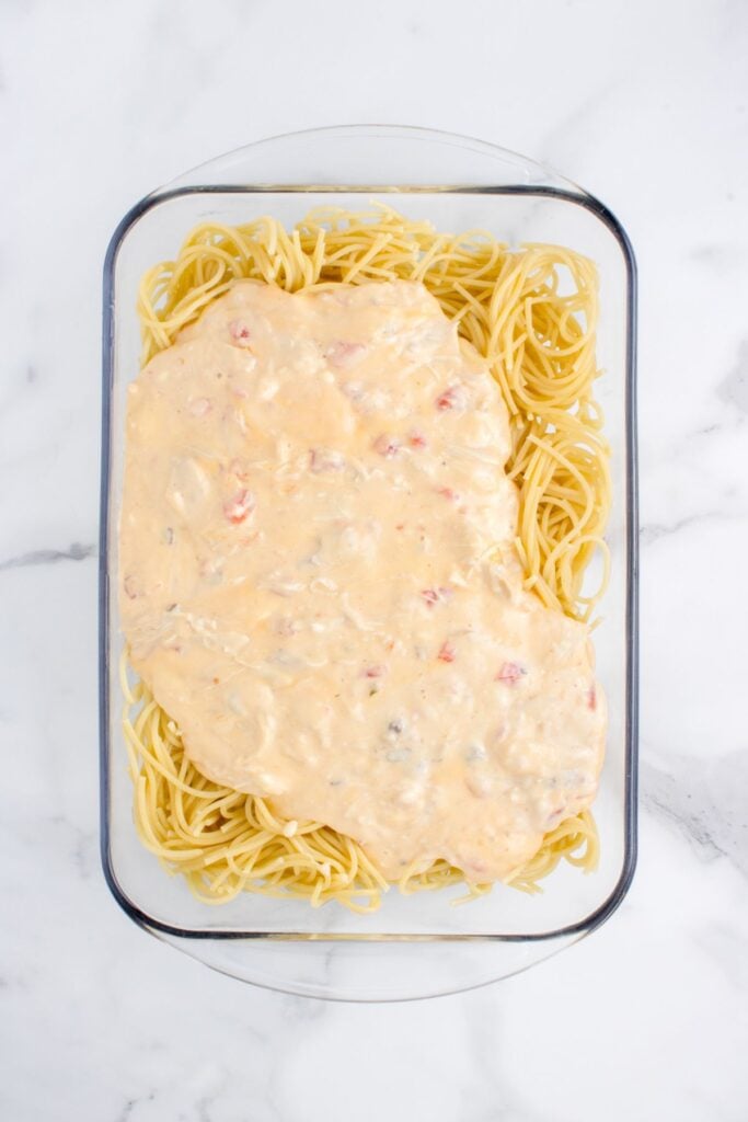 adding creamy cheese and chicken mixture to cooked spaghetti