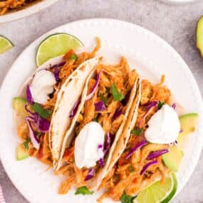 overhead picture of pulled chicken tacos on a white plate with limes