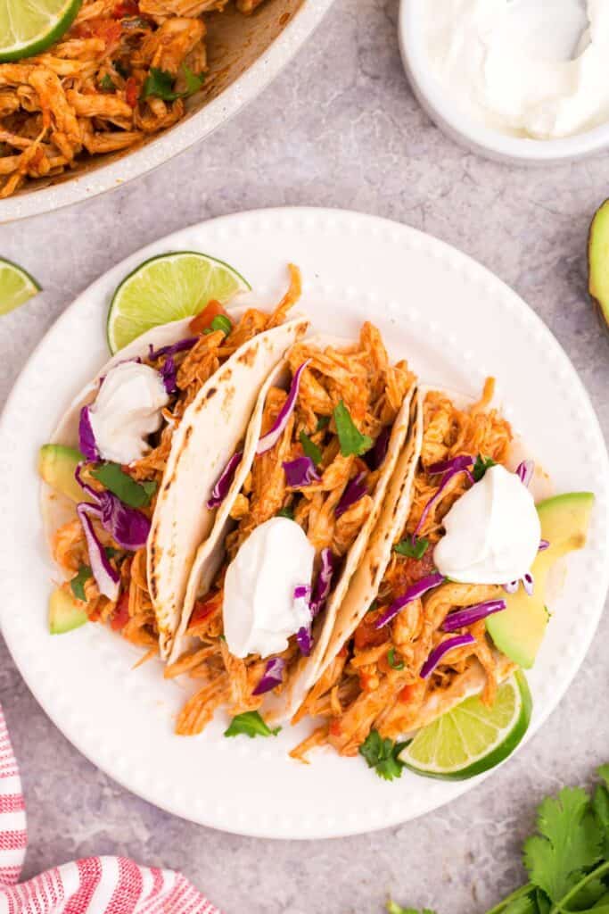 overhead picture of pulled chicken tacos on a white plate with limes