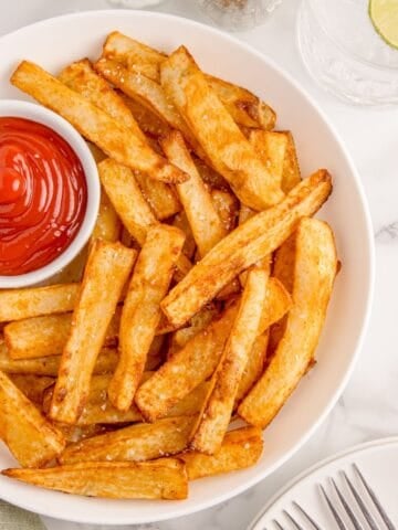 Air fryer french fries on a white plate served with ketchup.