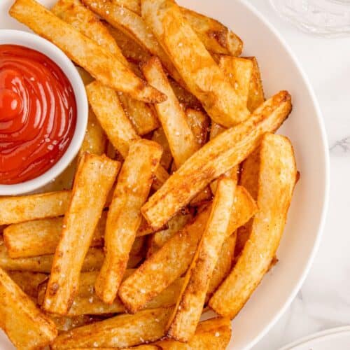 Air fryer french fries on a white plate served with ketchup.