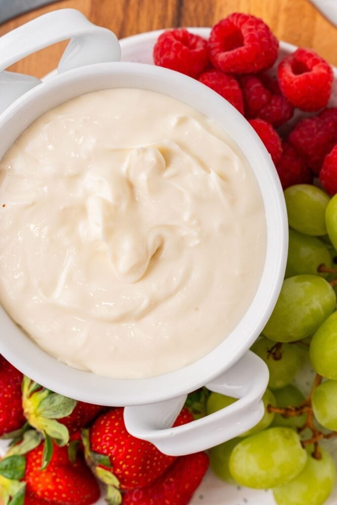 Fruit dip recipe in a bowl served with strawberries, grapes, and raspberries around it.