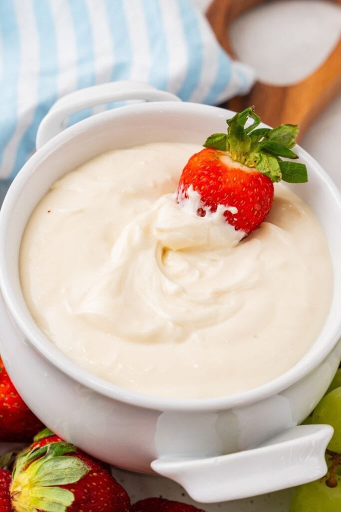 My cream cheese fruit dip recipe in a bowl with a strawberry in it with the dip on half of it.