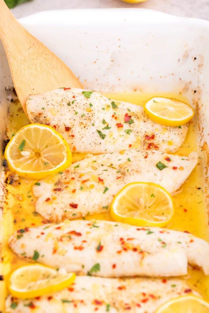 Spatula about to pull out the baked tilapia from the baking dish.