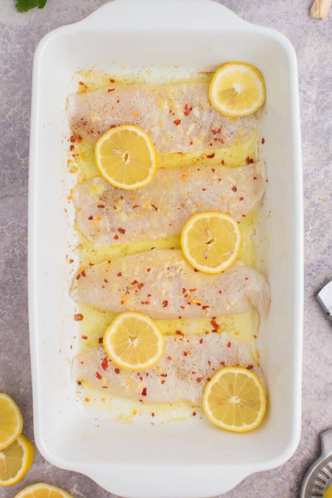 Raw tilapia in a pan with lemons about to be placed in the oven.