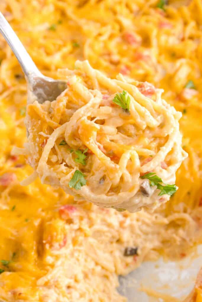 Chicken spaghetti with Rotel scooped up onto a spoon with the casserole filled with it in the background.