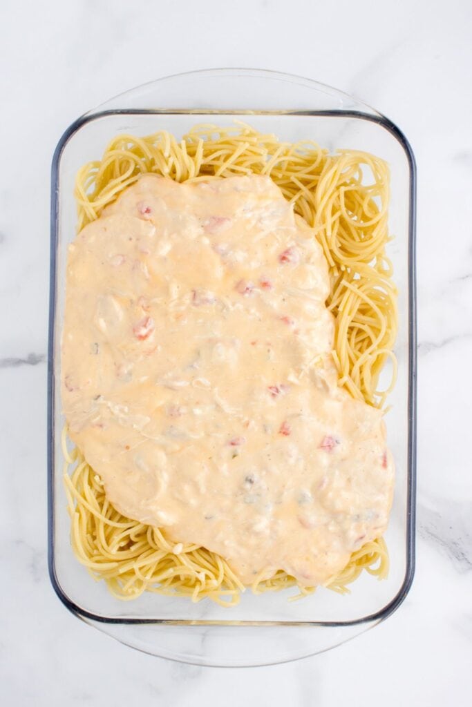 The cheese and chicken being spread over the spaghetti in a casserole dish before it's been baked.