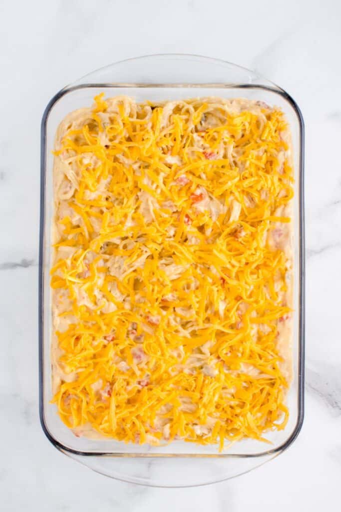 Chicken spaghetti casserole with extra cheddar cheese spread on top, ready to go in the oven.