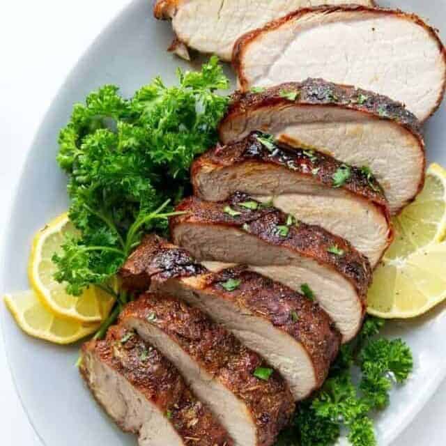 Air Fryer Pork Loin sliced on a plate with parsley and lemons