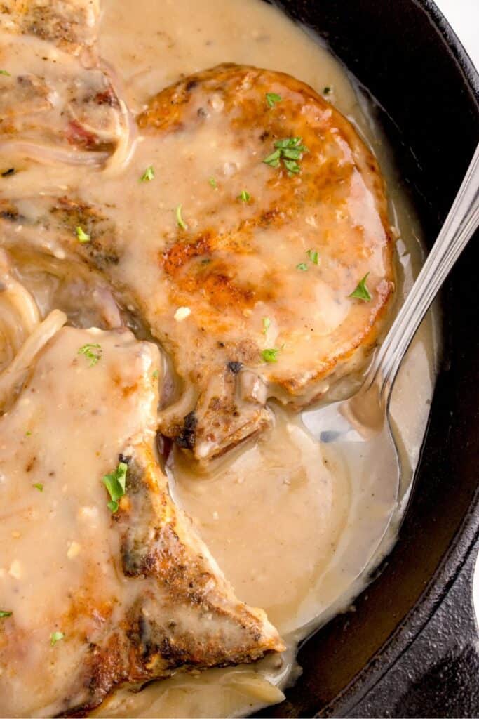 Close up of smothered pork chops in a cast iron pan with gravy.