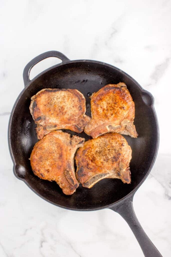 Pan fried pork chops in a cast iron pan.