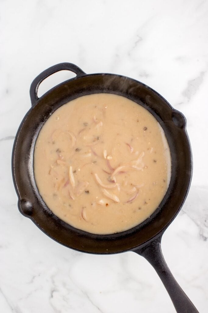 Onion mushroom gravy being cooked in a cast iron pan.