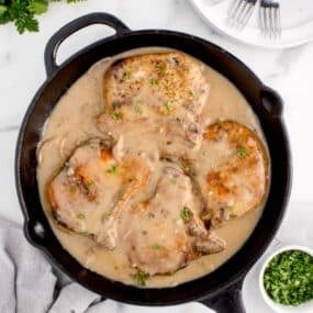 Fully cooked pork chops and gravy in a cast iron skillet.