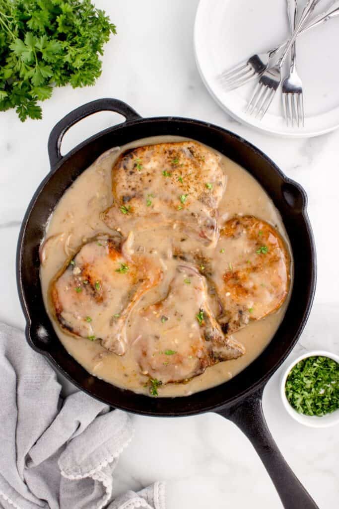 Fully cooked pork chops and gravy in a cast iron skillet.