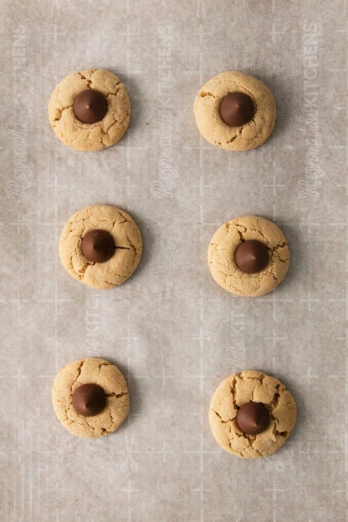 Peanut butter cookies with kisses on a baking sheet with parchment paper after they were baked.