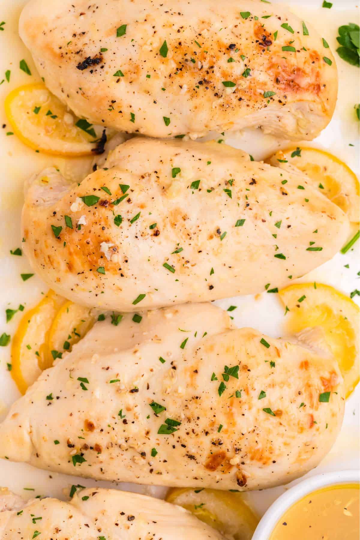Lemon butter chicken with lemon slices on a white serving dish.