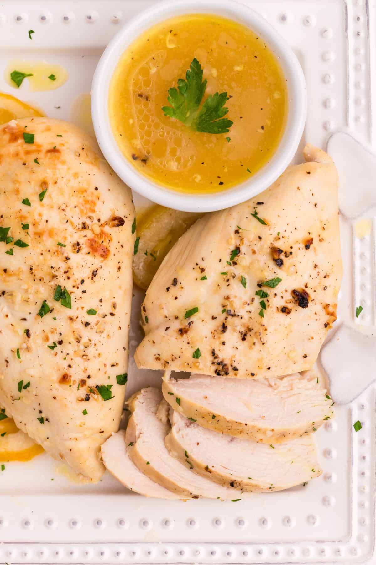 Lemon butter chicken on a serving platter with one chicken breast half sliced up.