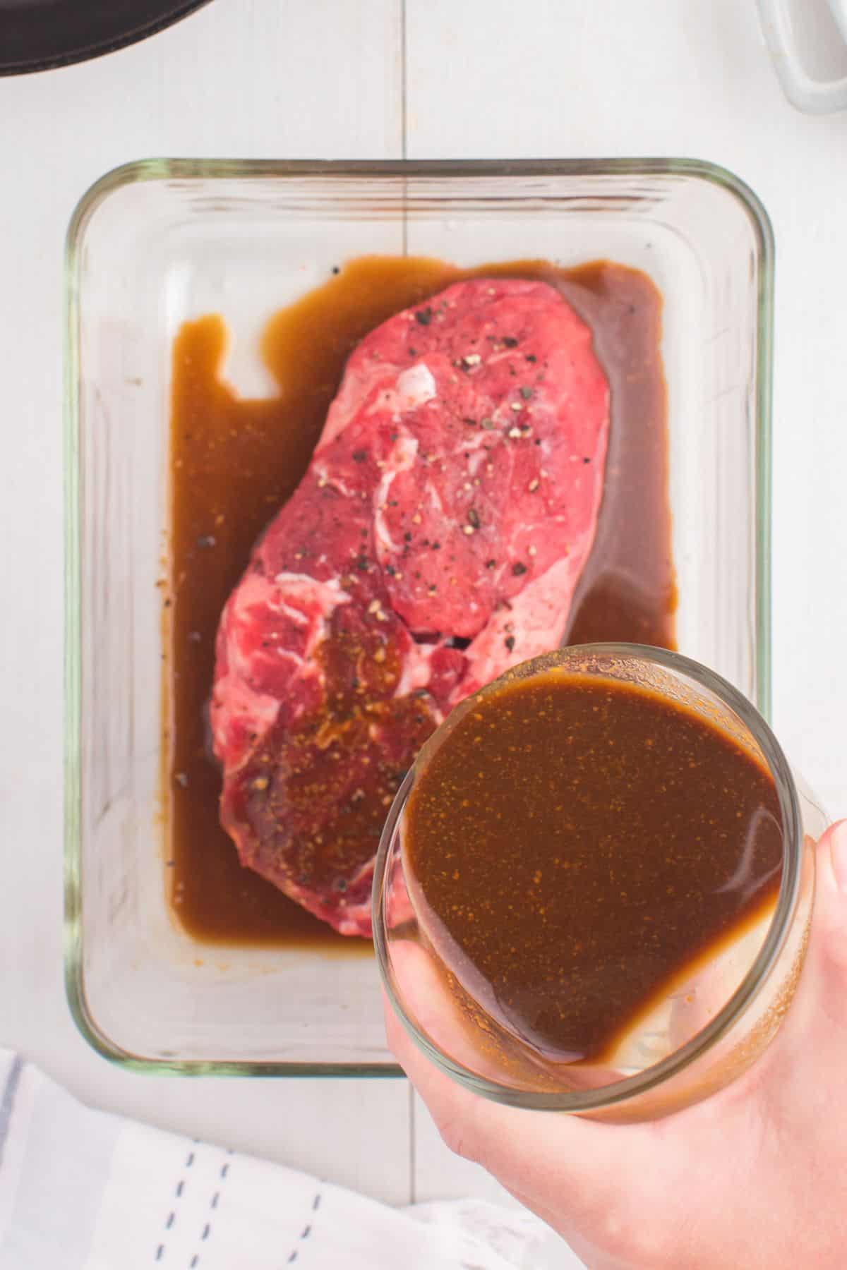 Marinade being poured over a steak in a glass dish.