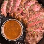 Overhead view of medium rare cooked steak that's sliced, next to a small bowl of easy steak marinade.