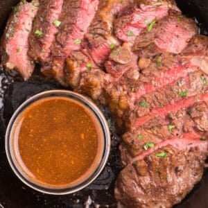 Overhead view of medium rare cooked steak that's sliced, next to a small bowl of easy steak marinade.