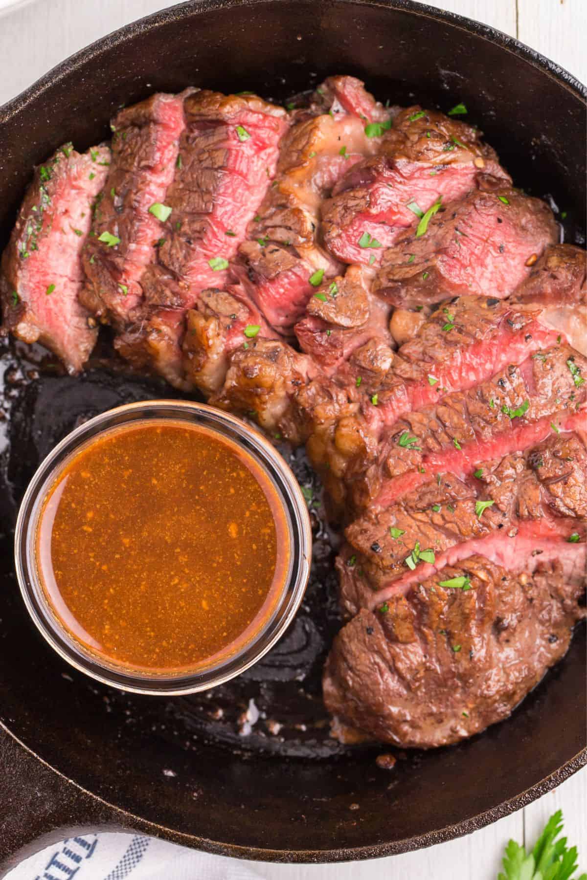 Overhead view of medium rare cooked steak that's sliced, next to a small bowl of easy steak marinade.