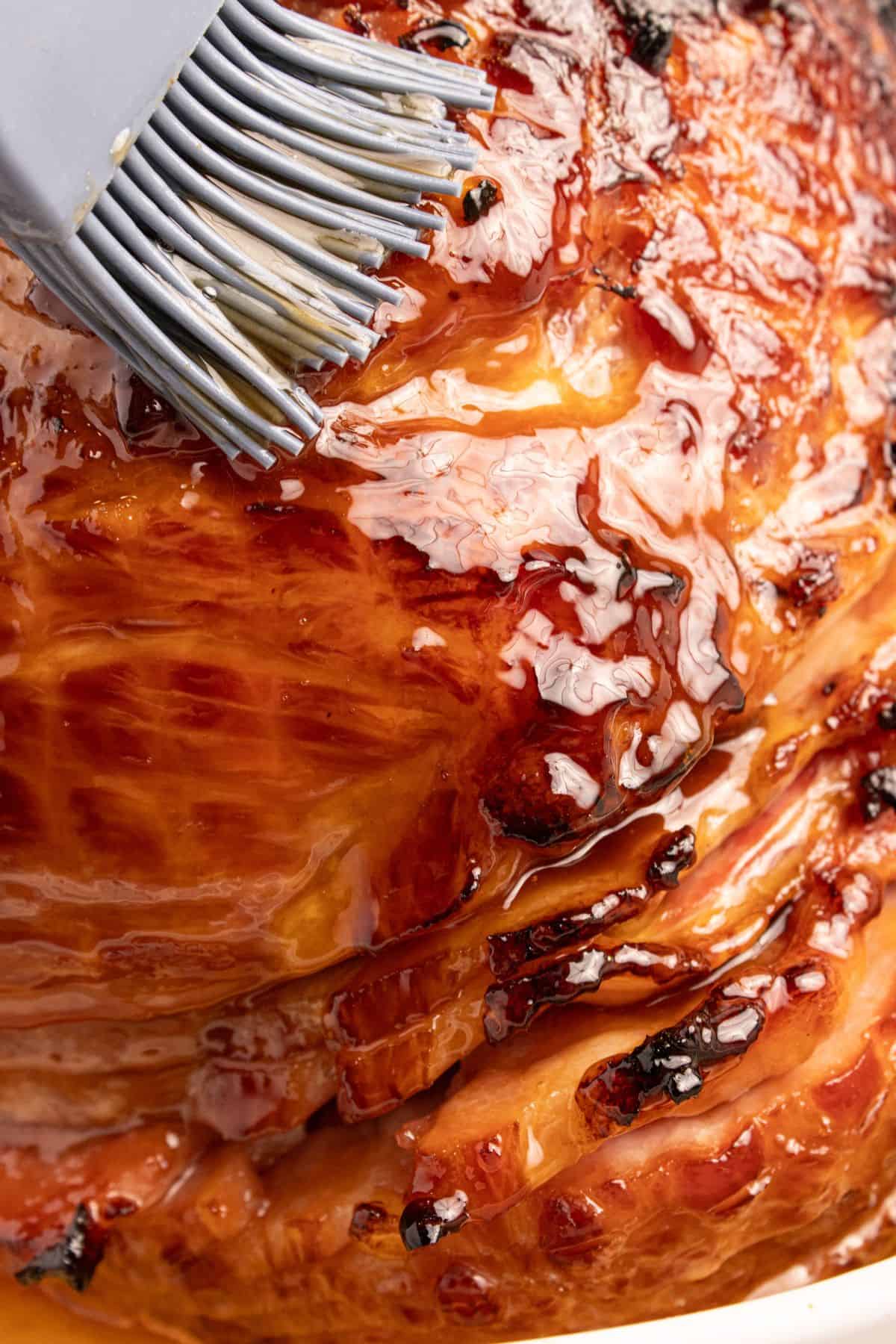 Close up of the 3-ingredient ham glaze being basted on ham with some caramelization and stickiness showing.