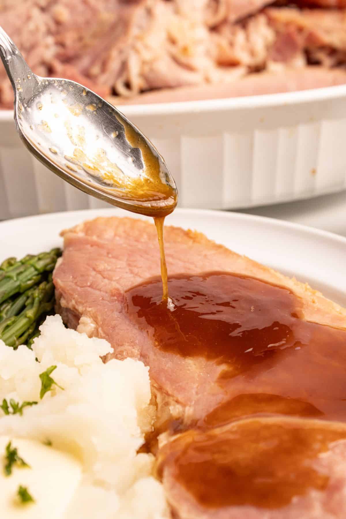 Easy ham glaze being spooned onto a piece of ham for extra flavor.