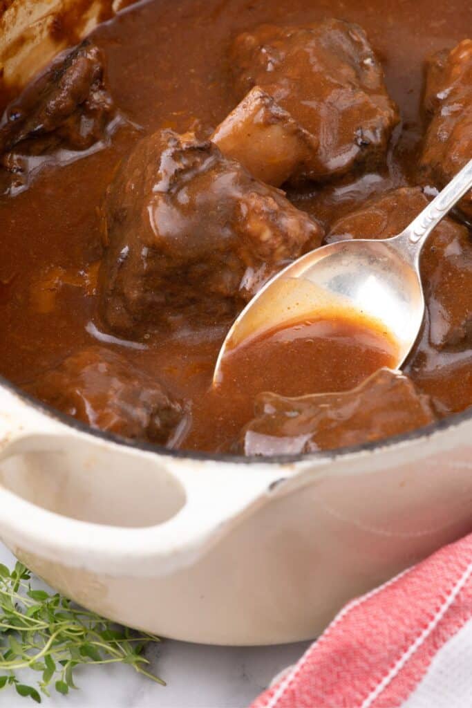 Large dutch oven with short ribs and a serving spoon.