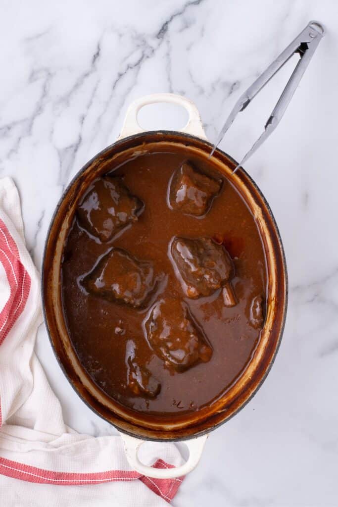 Dutch oven of braised short ribs and a pair of tongs.