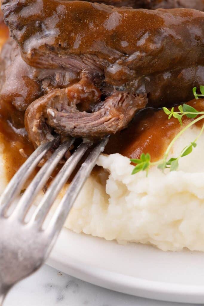 Close up of a fork removing a bite of short ribs from the dinner plate.
